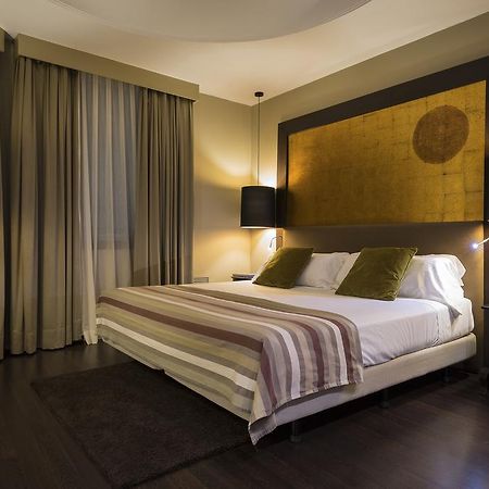 Only You Hotel Valencia Exterior foto The photo shows a modern bedroom that features a large bed with two green accent pillows and a striped bedspread. The room has a warm, neutral color scheme, highlighted by soft lighting from two bedside lamps. The wall behind the bed has an artistic 